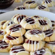Side view of raspberry almond thumbprint cookies piled on white round plate.