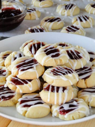 Side view of raspberry almond thumbprint cookies piled on white round plate.