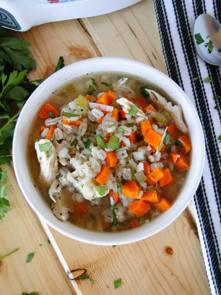 Top view of crock pot chicken barley soup in white bowl.