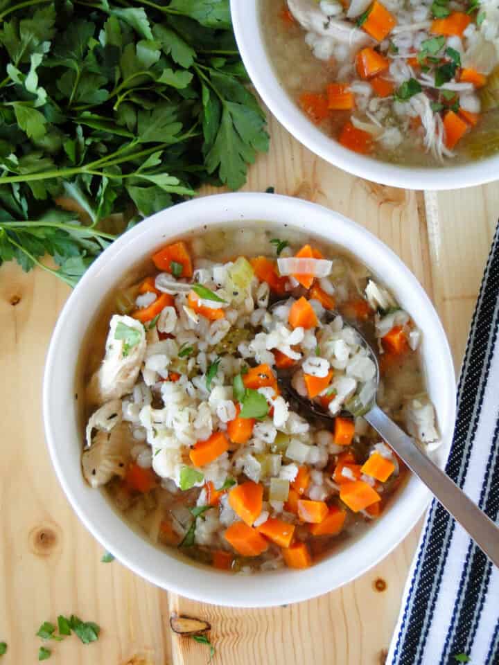 Top view of crock pot chicken barley soup in white bowl with spoon in bowl.