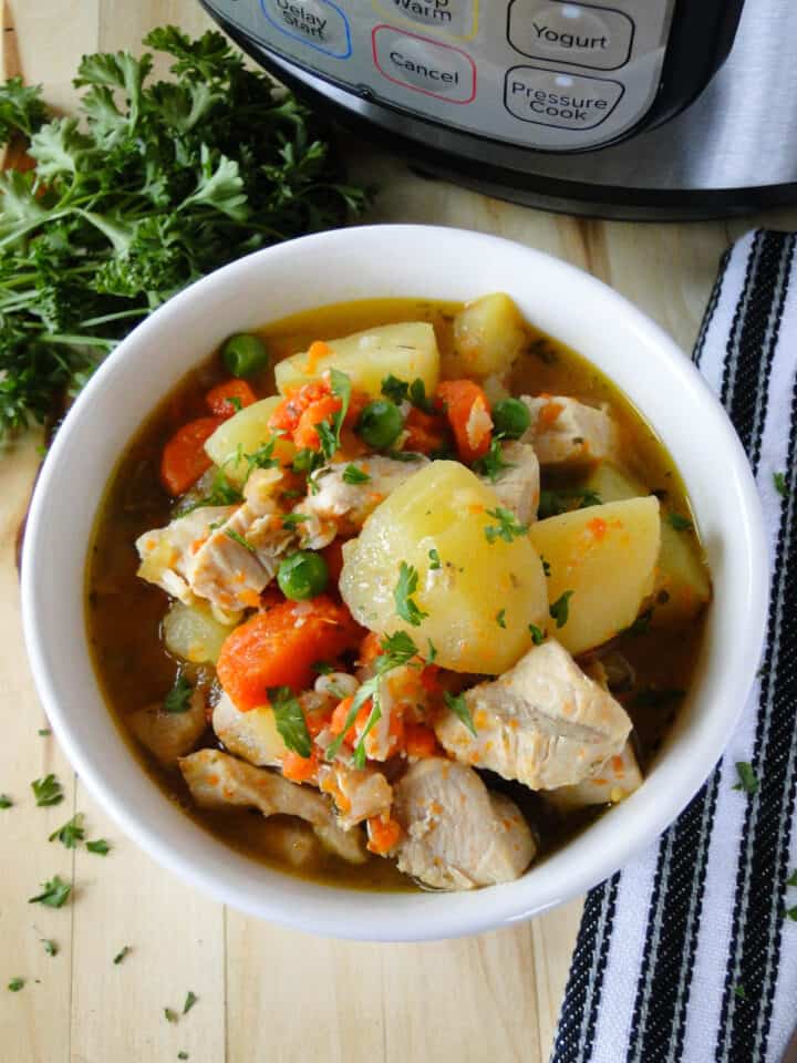 Close up view of instant pot chicken stew in white bowl in front of instant pot.