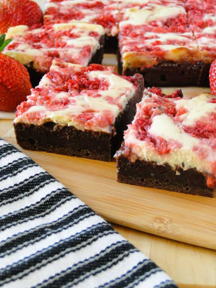 Close up side view of two sliced strawberry cheesecake brownies on small board.