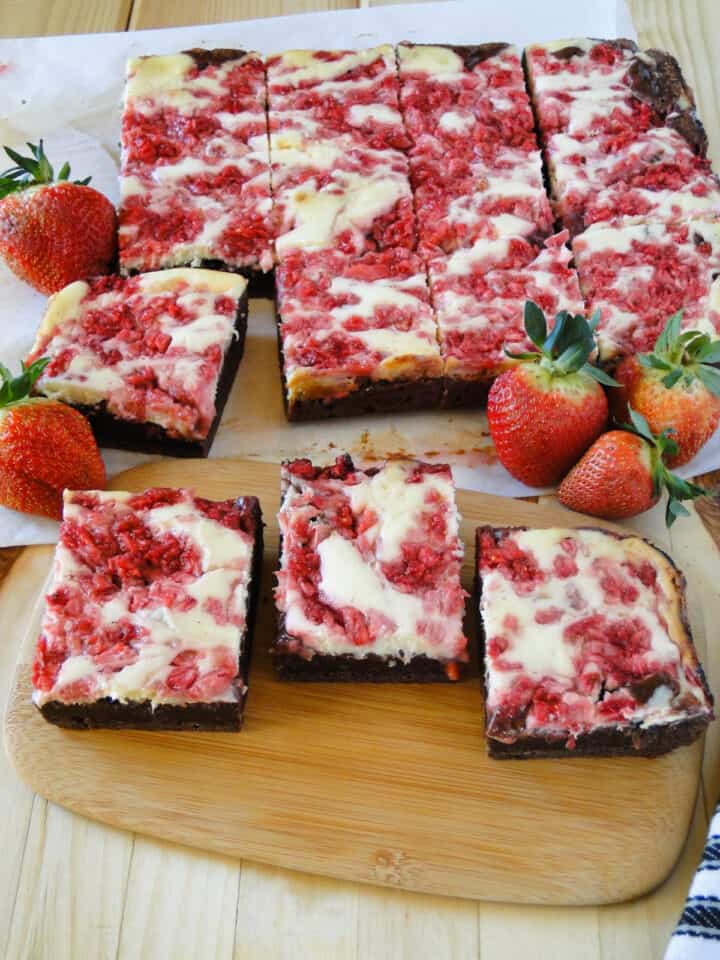 Strawberry cheesecake brownies sliced and in rows with 3 separate in front and fresh strawberries around.