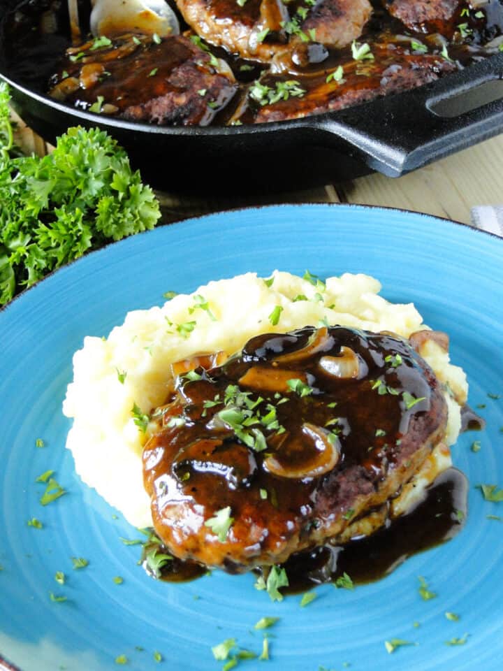 Turkey Salisbury steak on top of mashed potatoes on round blue plate.