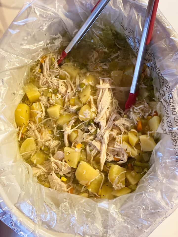 Cooked soup and chicken broken apart and shredded.