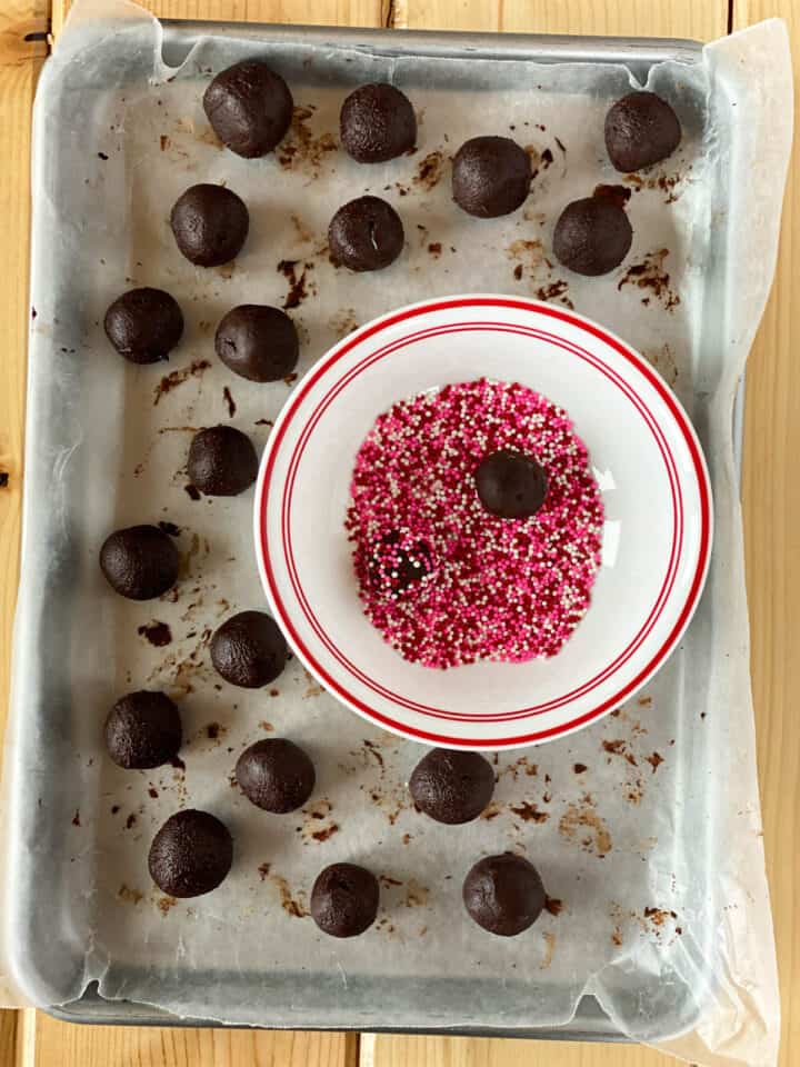 Rolled truffles on sheet pan with bowl of sprinkles.