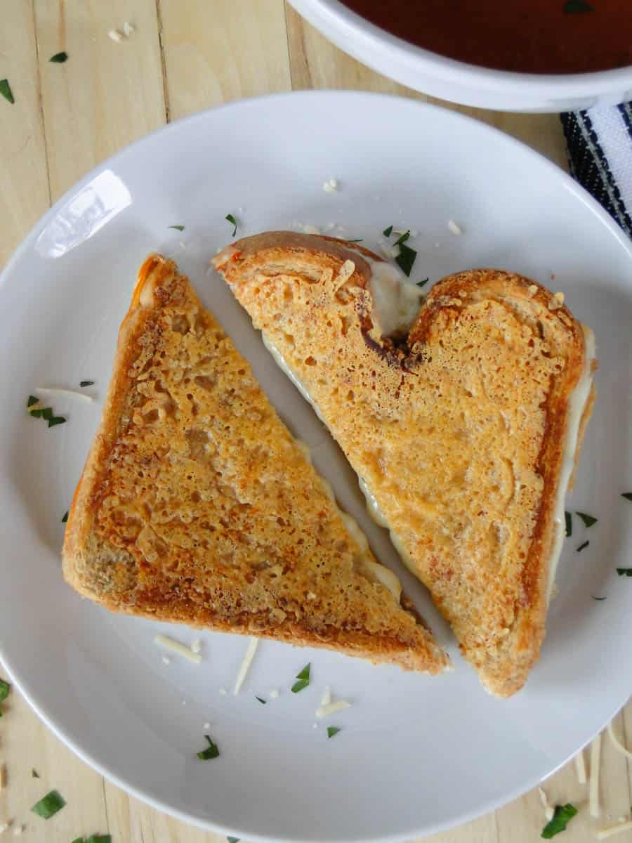 Parmesan crusted grilled cheese cut in half on white round plate.