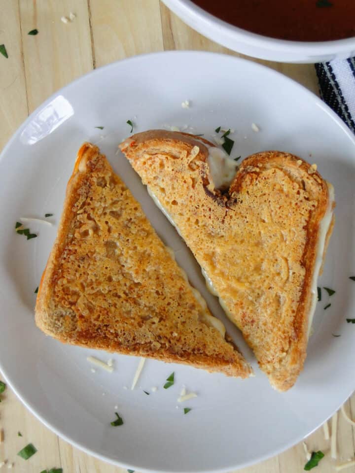 Parmesan crusted grilled cheese cut in half on white round plate.