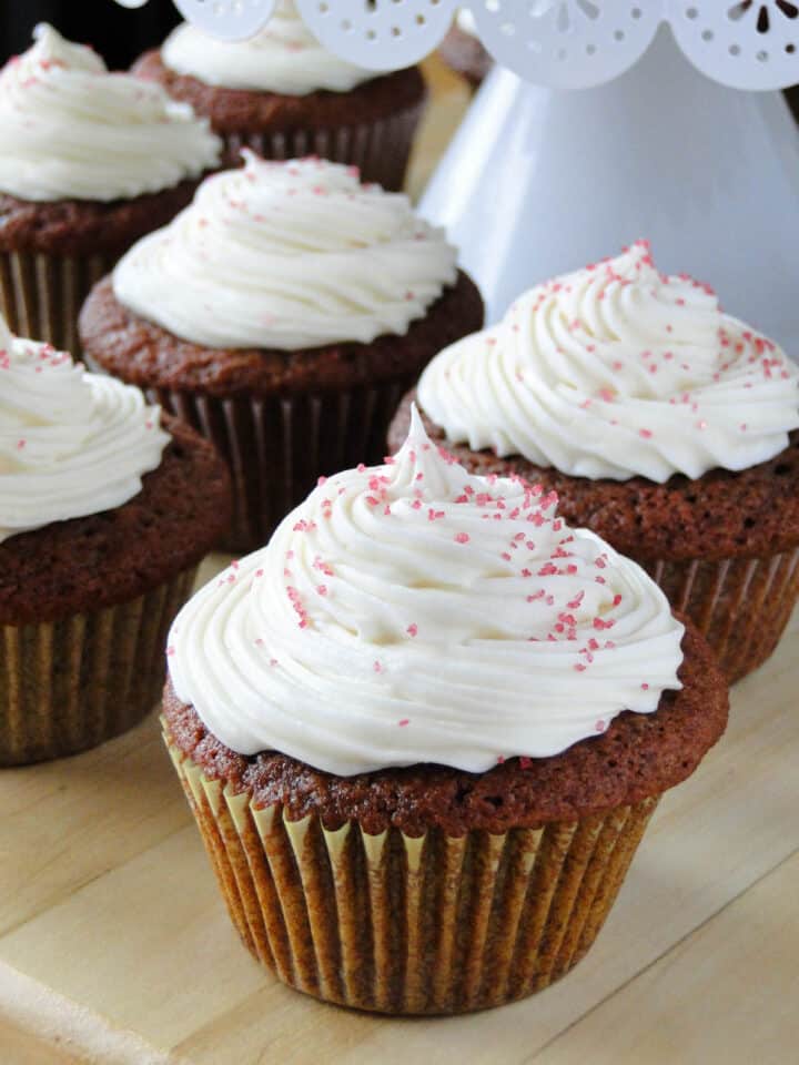 Red velvet cupcakes with cream cheese frosting in rows under cake stand.