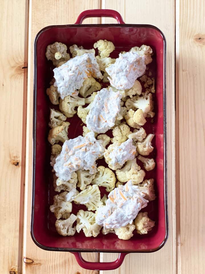 Roasted cauliflower in casserole dish dolloped with cheese mixture.