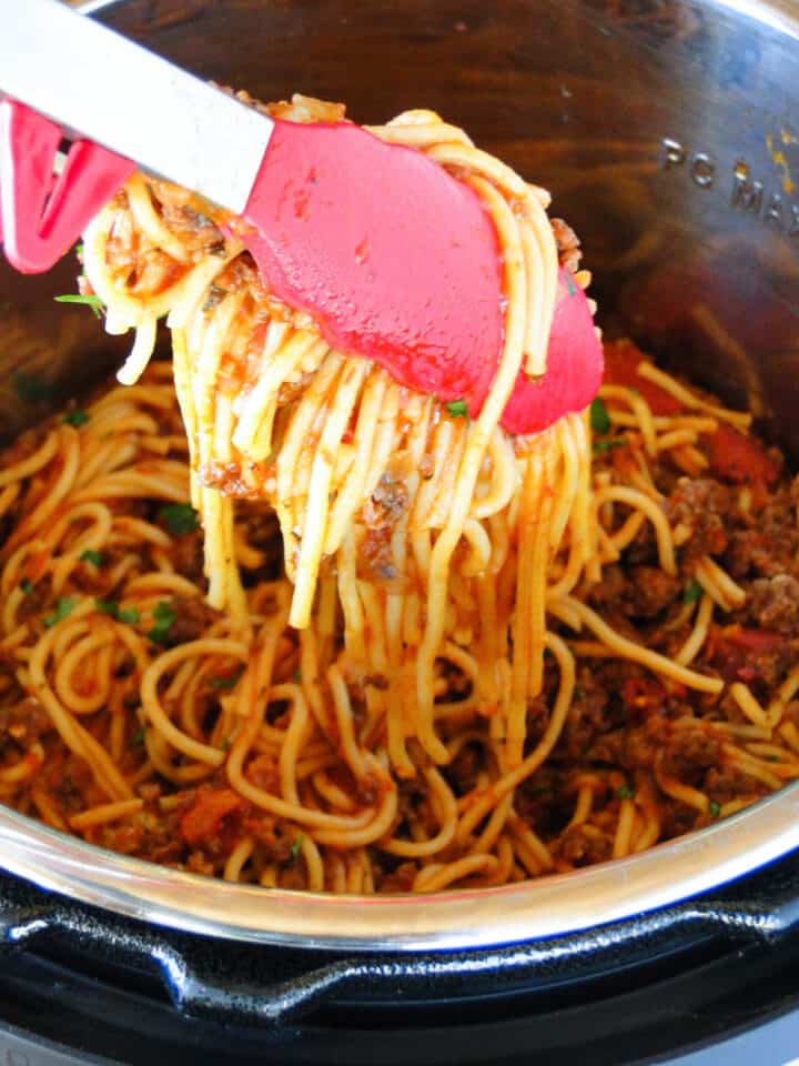 Instant pot spaghetti and meat sauce being dished out of instant pot with red tongs.