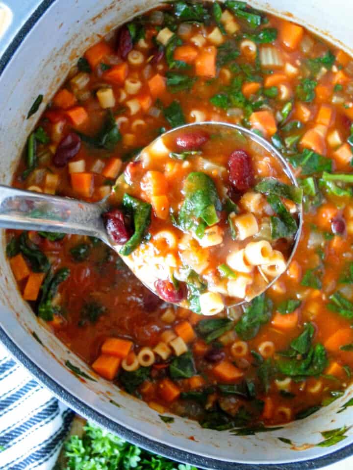 Ladleful of Italian minestrone soup being served out of soup pot.