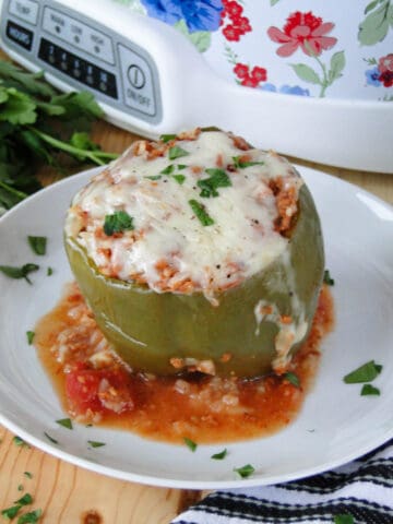 Crock pot stuffed pepper topped with melted cheese on white round plate.