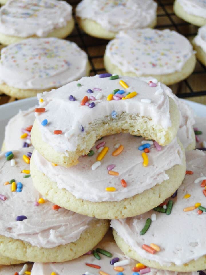 Easy frosted sugar cookies on a plate with bite taken out of top cookie.