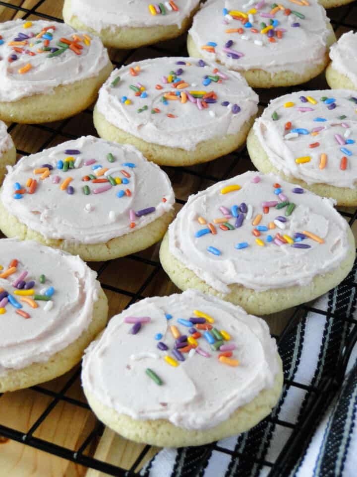 Frosted sugar cookies with sprinkles in rows on wire rack.