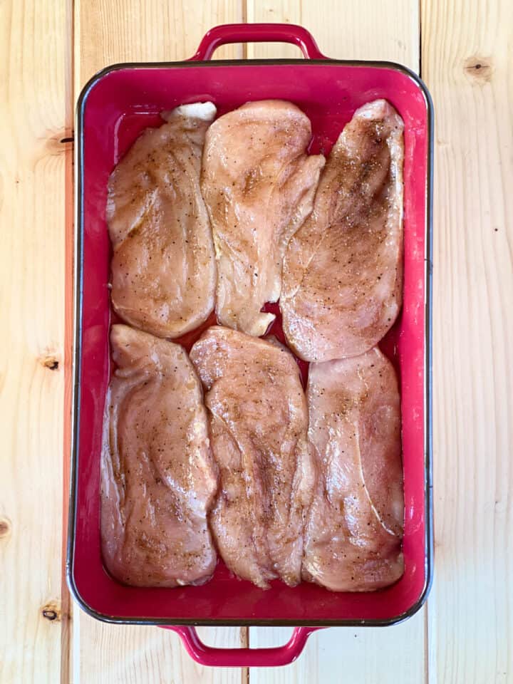 Seasoned chicken in red casserole dish ready for the oven.