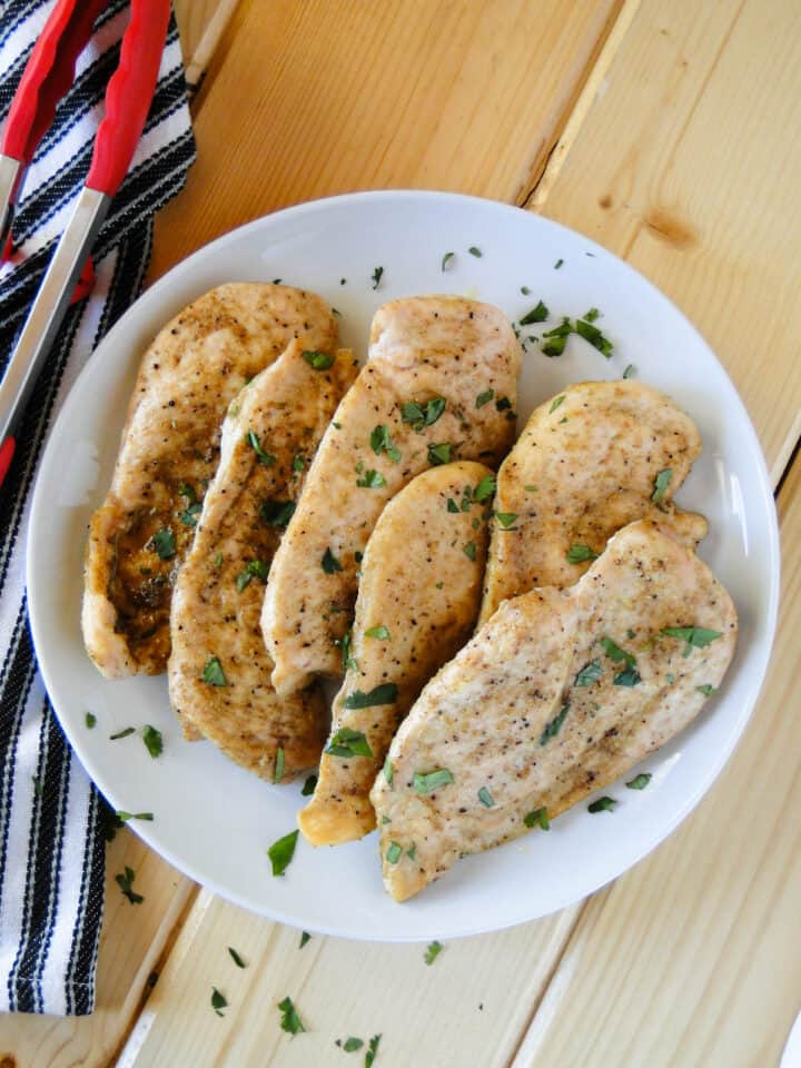 Baked cumin chicken breasts on white serving plate next to red tongs.