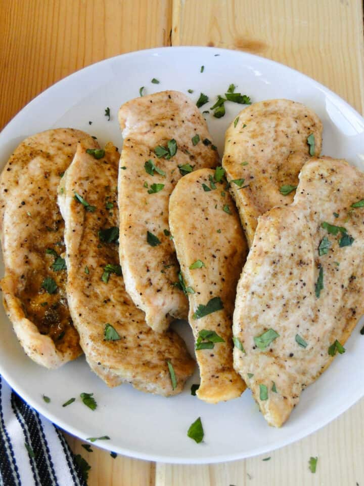 Close up view of baked cumin chicken breasts on serving plate.