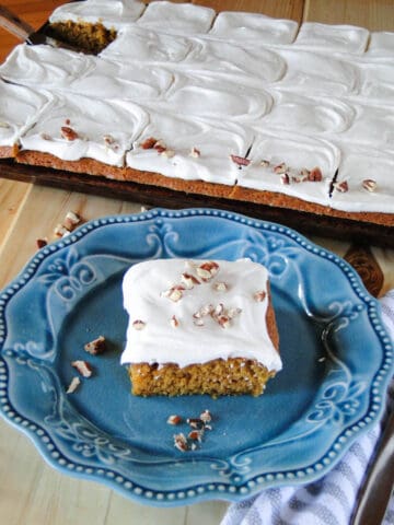 Top view of easy carrot cake slice on blue plate in front of entire pan of sheet cake.