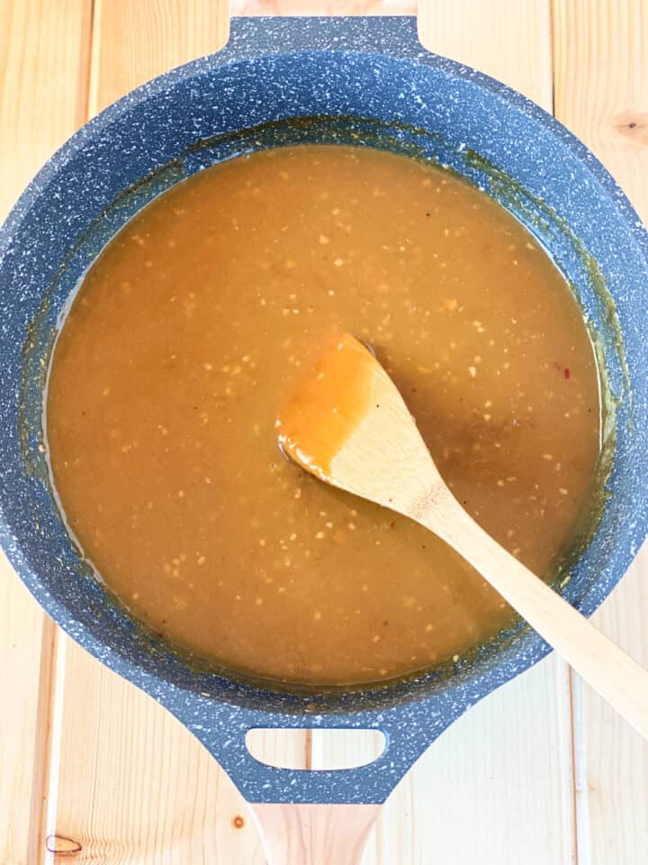 Orange sauce in large round skillet with wooden spoon.