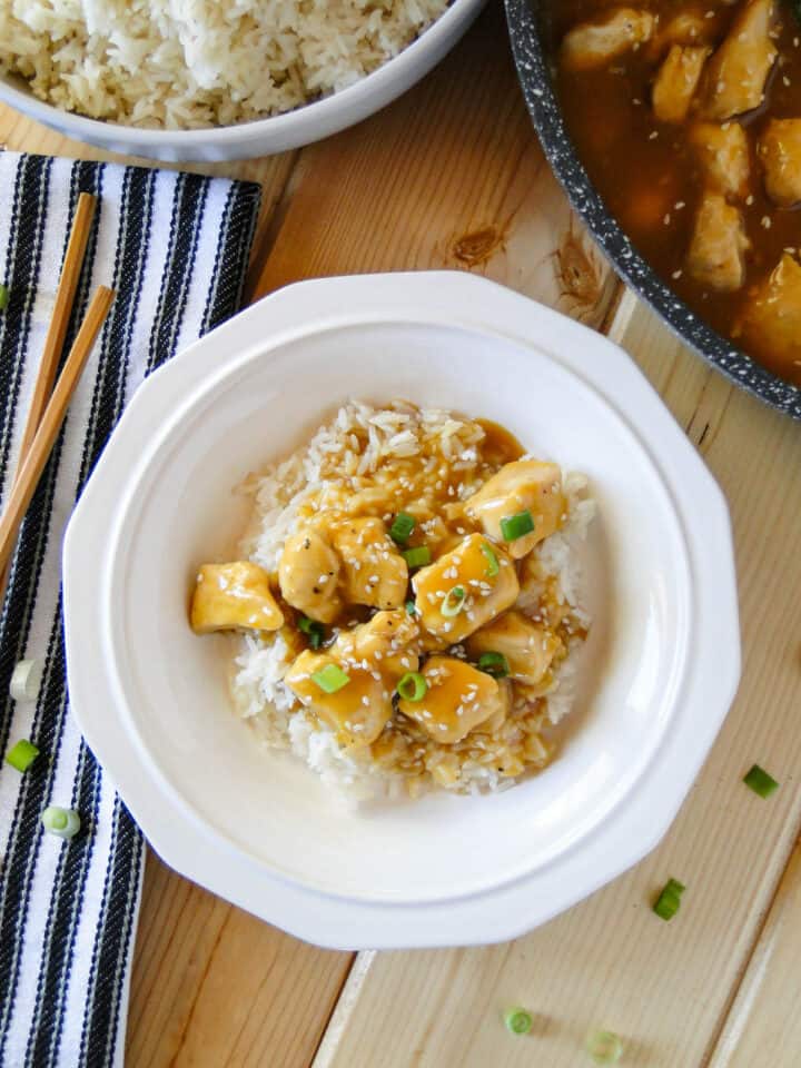 Easy orange chicken served over rice in white round bowl.