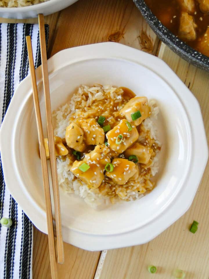 Close up view top view of easy orange chicken served over rice in white round bowl with chopsticks.
