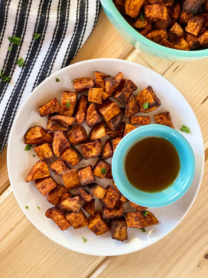 Air fryer cinnamon sweet potatoes on round with plate with small bowl of maple syrup. 