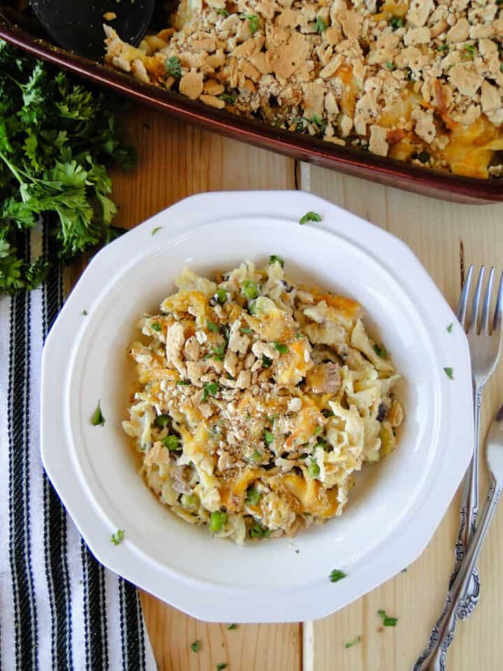 Top view of tuna noodle casserole in white round bowl in front of casserole dish.