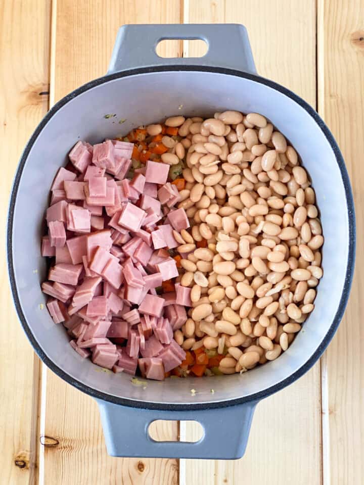 Canned beans and diced ham added to cooked veggies and seasonings in large soup pot.