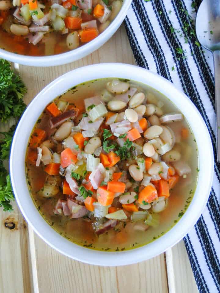 Close up of ham and bean soup in white round bowl.