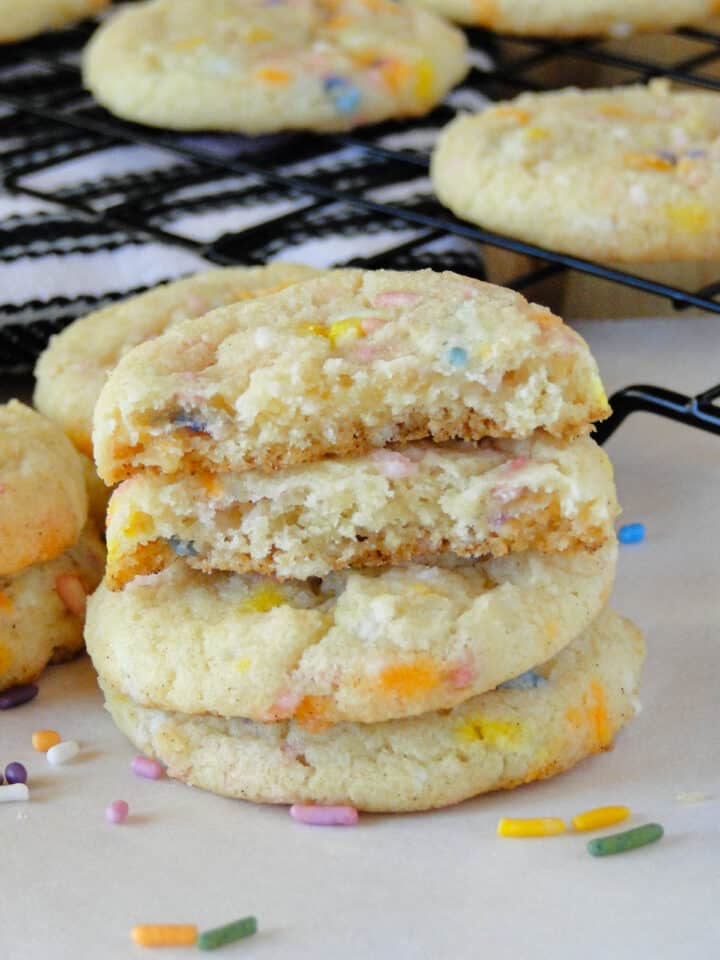 Stack of 3 confetti sugar cookies with the top cookie broken in half showing chewy center.