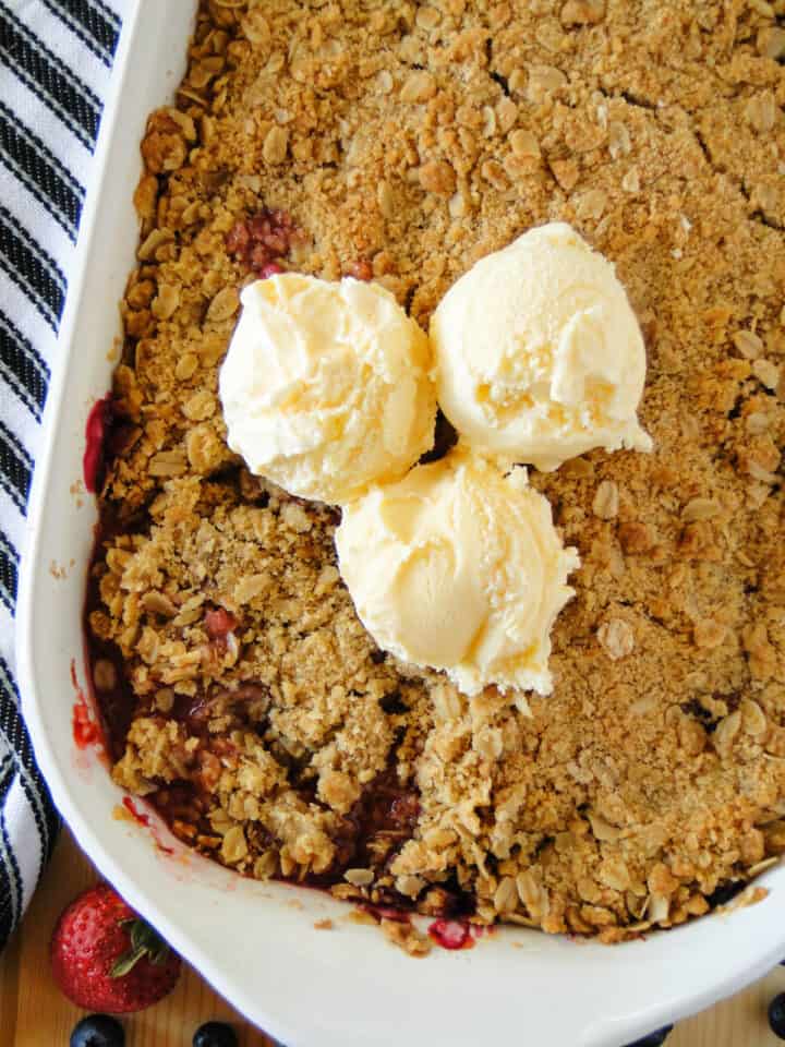 Triple berry crisp in baking dish topped with three scoops of ice cream.