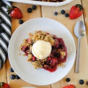 Top view of triple berry crisp served on white round plate topped with a scoop of ice cream.