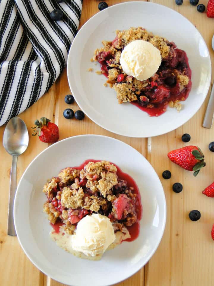 Top view of triple berry crisp served on white round plates topped with a scoop of ice cream.