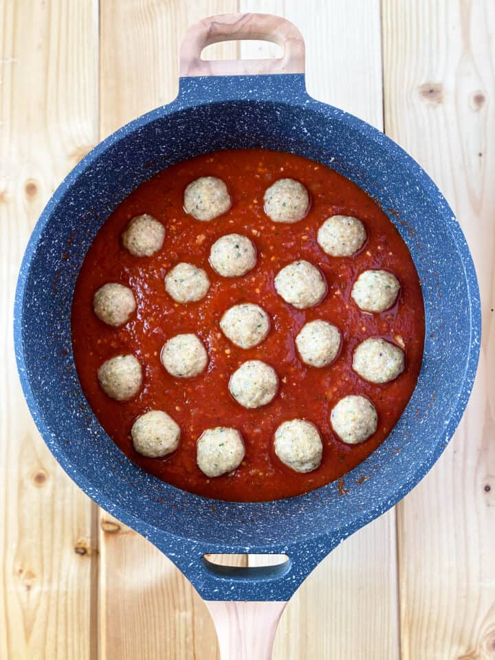 Baked meatballs added to simmering red sauce in large sauce pan.