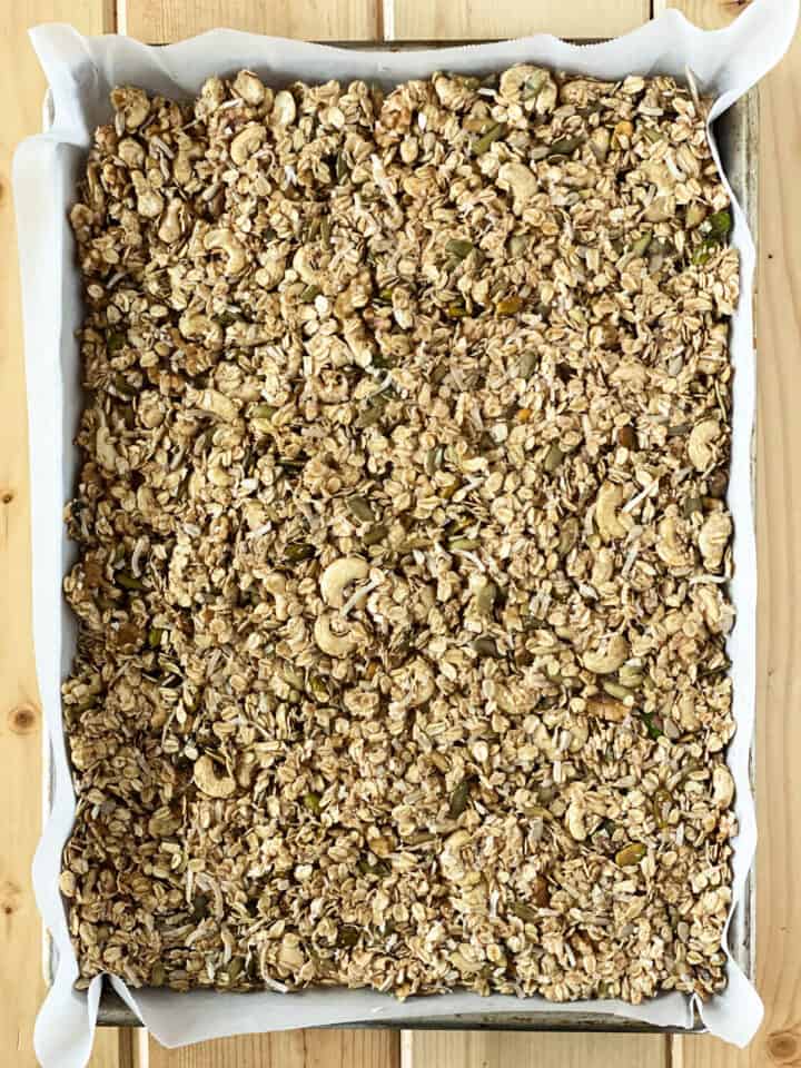Granola spread out on parchment lined sheet pan.