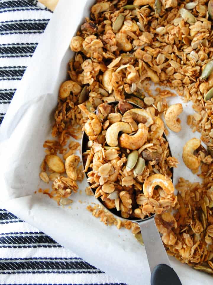 Homemade granola in measuring cup on sheet pan with more granola.