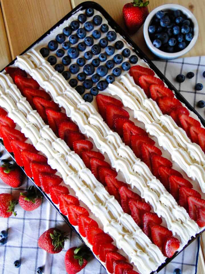 Top view of American flag cake in sheet pan with strawberries and blueberries.