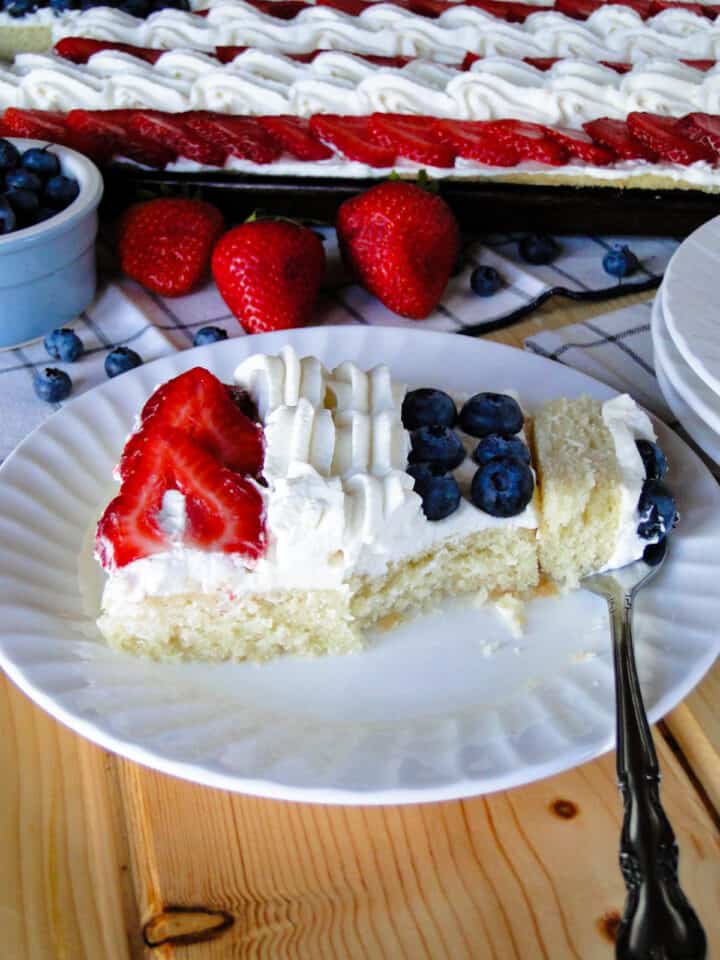 Slice of American flag cake on white round plate with a bite on a fork.