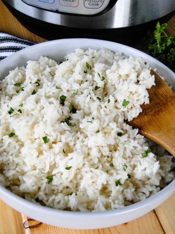 Instant pot white rice in white round bowl with wood serving spoon.