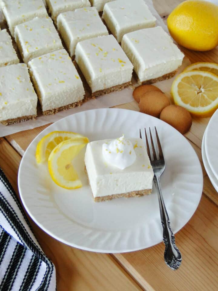 No bake lemon cheesecake bar topped with whipped cream on white round plate with fork.