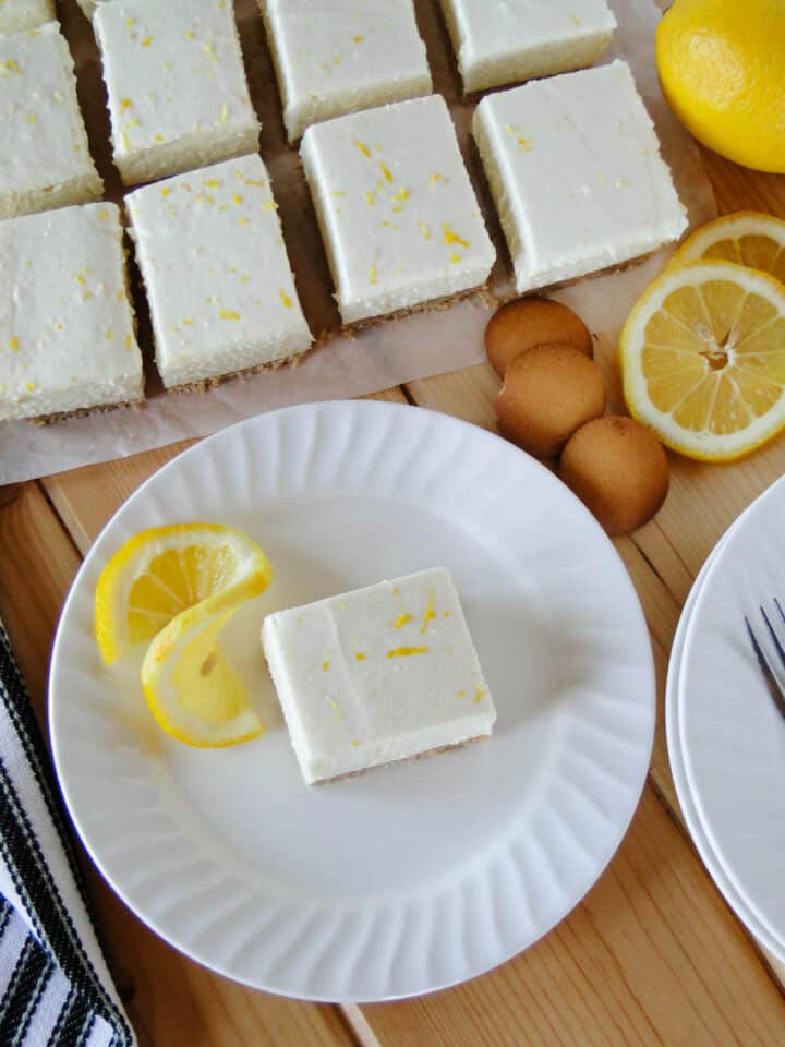 No bake lemon cheesecake bar topped with on white round plate in front of of more bars.