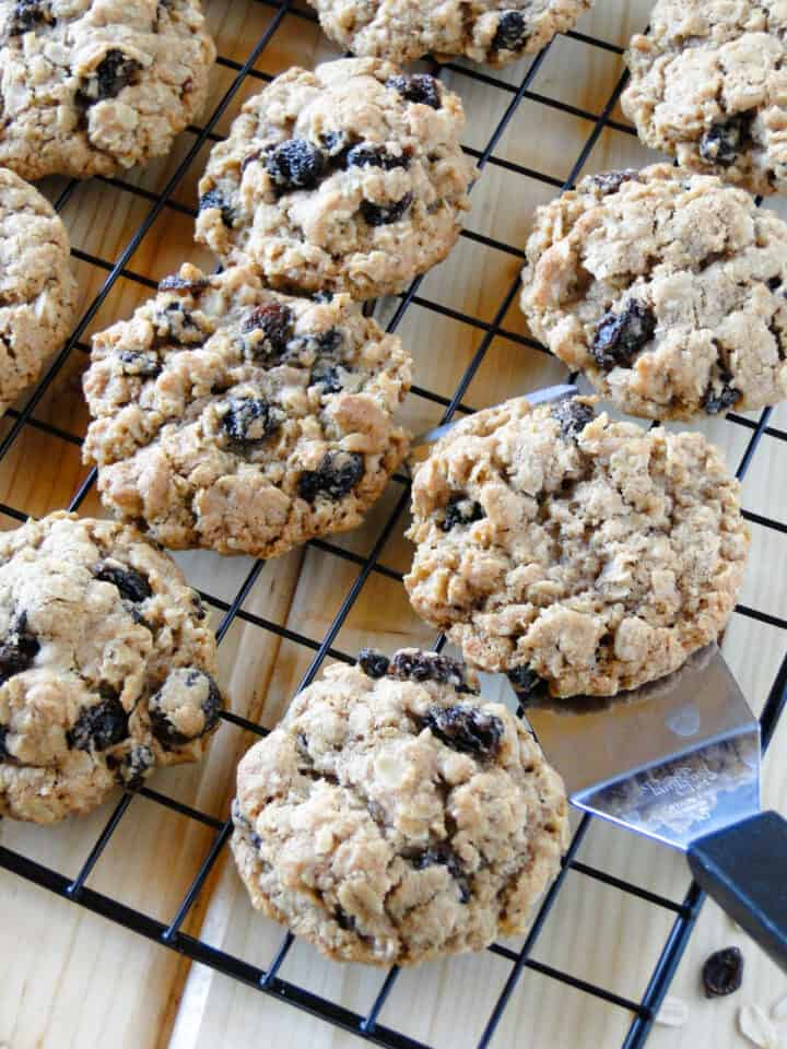 Oatmeal raisin cookies in rows on wire rack with a small spatula under one cookie.