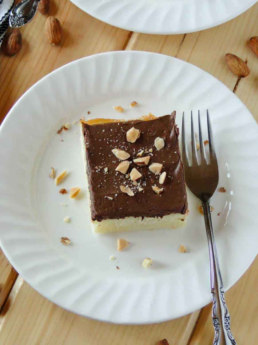 Top view of almond cake with chocolate frosting on white round plate with fork.