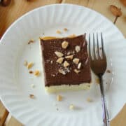 Top view of almond cake with chocolate frosting on white round plate with fork.