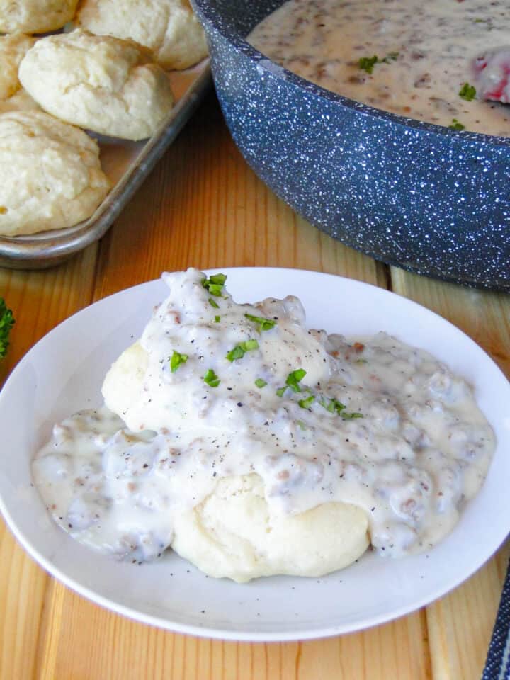 Close up side view of biscuits and sausage gravy on white plate.