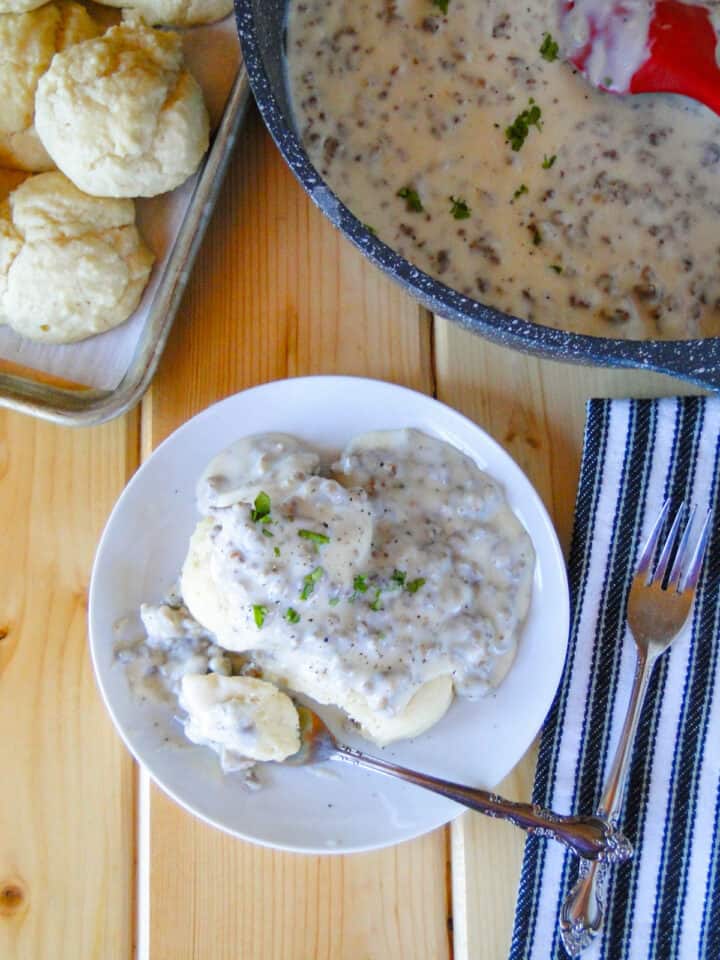 Biscuits and Sausage gravy on white round plate with bite on fork.