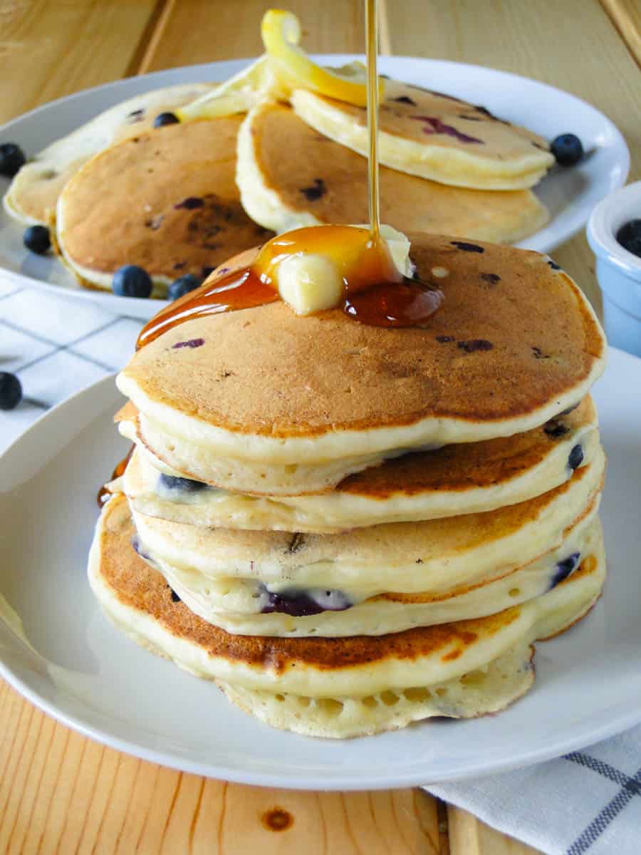 Stack of blueberry lemon ricotta pancakes with drizzle of maple syrup over top.