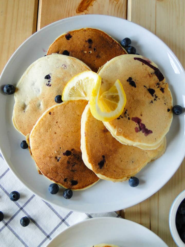 Platter of blueberry lemon ricotta pancakes with lemon slice swirl on top.