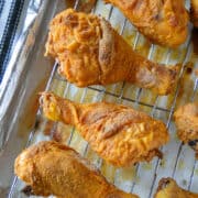Close up view of oven fried chicken legs on wire rack in pan.